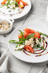 Healthy vegetable salad with fresh arugula, tomato, feta cheese on white plate with cutlery, gray tile background. Diet menu. Appetizer salad