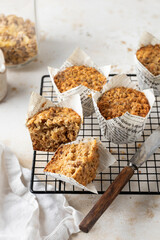 Morning breakfast oatmeal muffins in white paper cups on cooling rack with knife on white textured background