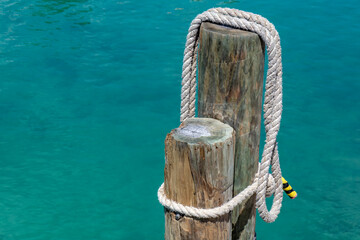 Overhead view of a rope draped over wooden poles on a dock to tie up a boat.  Turquoise water in...