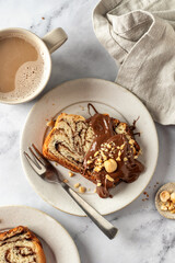 Slice of brioche babka bread with chocolate filling on white marble background served with chocolate and nuts and a cup of coffee. Easter traditional baking top view