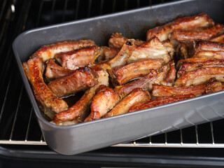 Tasty baked pork ribs in a black baking tray in an oven.