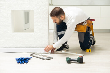 The craftsman measures the length of the plinth for cutting, installing the plinth on the corner of...