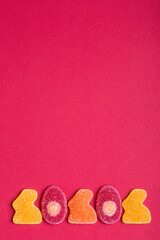 Jelly Easter sweets in form of bunny and egg in orange, red and yellow colors on red cardboard backdrop. Easter card, copy space, selective focus.