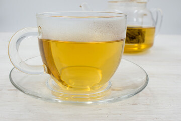 Brewed green tea poured into a glass cup and a teapot on wooden table.