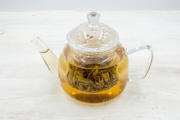 Green tea brewed in a glass teapot on a wooden white table.