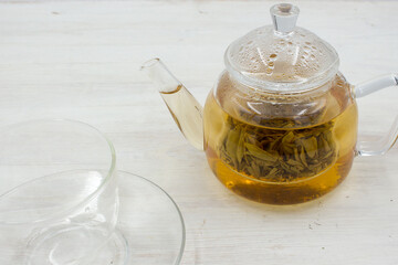 Green tea brewed in a glass teapot on a wooden white table.
