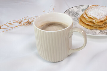 Cup of coffee with delicate foamed milk with pancakes on white background. Breakfast homemade with sweets and coffee.