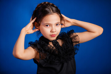 Fototapeta na wymiar Portrait of a little girl in a black dress with a pigtail hairstyle on her head poses, isolated on a dark background with blue backlight. 