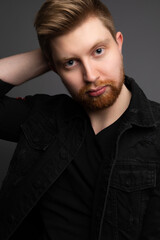 Obraz premium Studio portrait of a handsome caucasian male model. He is wearing a dark jacket and is posing. He is in his 20s and has blue eyes. The background is grey. 