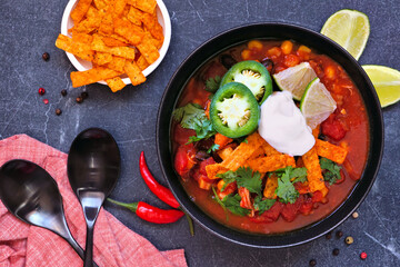 Chicken tortilla soup with tomatoes and black beans. Mexican food dish. Top view table scene on a dark background.