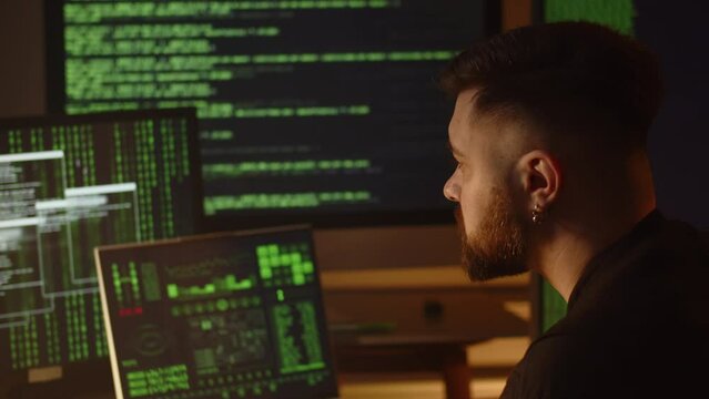 A data scientist analyzes data from monitors that display program code. A male programmer sits in the office and carefully examines the data from four monitors.