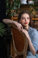 Close-up portrait of a brunette girl in a blue dress on a vintage chair