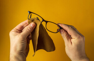 Close-up of a person's hands wiping dust off glasses with a napkin. Reading glasses on yellow...