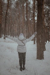 A beautiful young girl in a purple hat walks through a snowy forest in winter and smiles