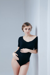 A young pregnant girl in a black bodysuit on a white background