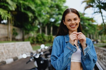 Fototapeta premium Portrait of a woman brunette smile with teeth walking outside against a backdrop of palm trees in the tropics, summer vacations and outdoor recreation, the carefree lifestyle of a freelance student.