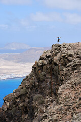 Woman with arms raised on top of a hill. With La Graciosa Island in the background