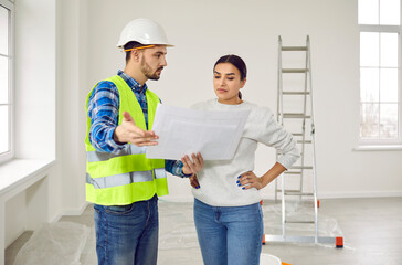 Foreman showing to a young homeowner woman design project or repair of her new apartment standing in empty white room. Meeting with builder about interior decoration or home layout. Moving concept.