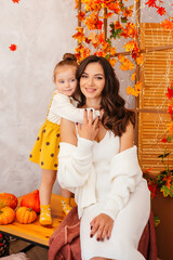 Mom and two little beautiful daughters in autumn with pumpkins and yellow leaves. Family cozy autumn day concept