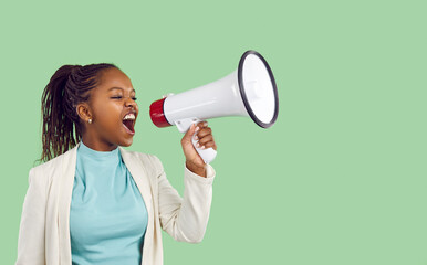Young woman with megaphone in her hand shouting advertising something on light green background. Woman shouts loudly announcing crazy discounts while standing near copy space. Advertising banner.