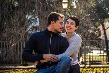 The young couple is sitting on a park bench in Rome. The beautiful couple in love is embracing