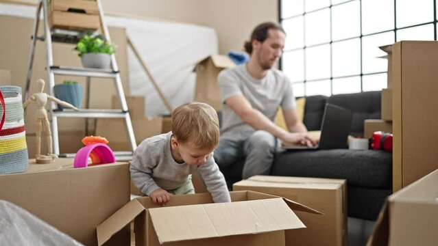 Father and son unpacking cardboard box using laptop at new home