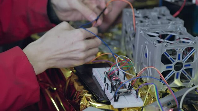 Electricians hands twists the wires from the spare part for the satellite printed on 3d printer