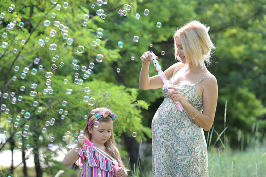 Little girl with her pregnant mommy have fun blowing bubbles