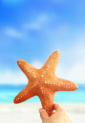 Fototapeta na wymiar Hand holding starfish with tropical summer beach island, relaxing vacation summer blue sea concept.
