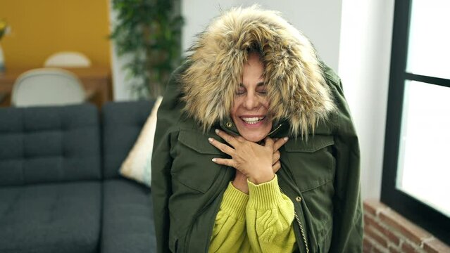 Middle age hispanic woman covering with jacket for cold sitting on sofa at home