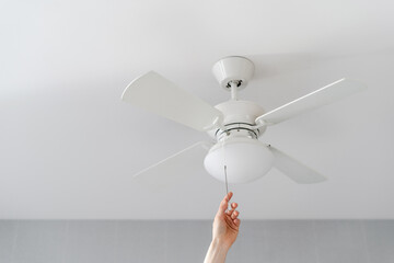 person turn on electric ceiling lamp with propeller indoors