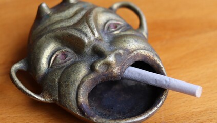 an old antique devil shaped ashtray with a cigarette in it