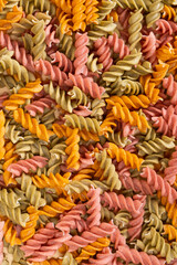 Rice vegetable pasta in the form of spirals, top view. Healthy rice pasta with tomatoes, selenera, carrots and beets