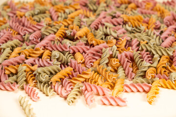 Rice vegetable pasta in the form of spirals on a white background. Healthy rice pasta with tomatoes, selenera, carrots and beets