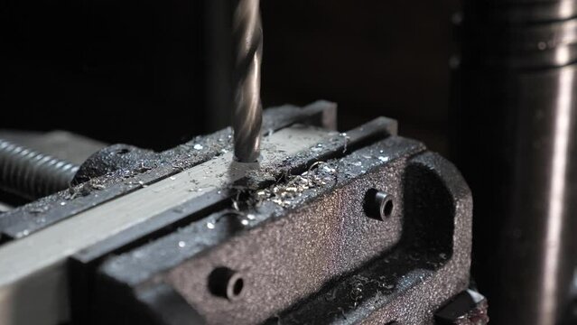 Locksmith workshop. Locksmith in workshop drills hole in metal workpiece. Drilling machine drills hole with bore in metal part. Mechanic at factory in workshop. Drilling machine. Worker drills hole.
