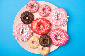 Many different donuts on a blue background top view, pink, white and chocolate donuts