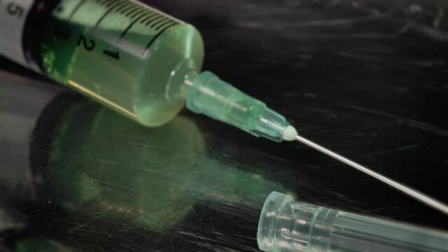 Green drug liquid inside a plastic syringe on a metal case, rotating in a b-roll video shot. Vaccination, research and medical social issues concept