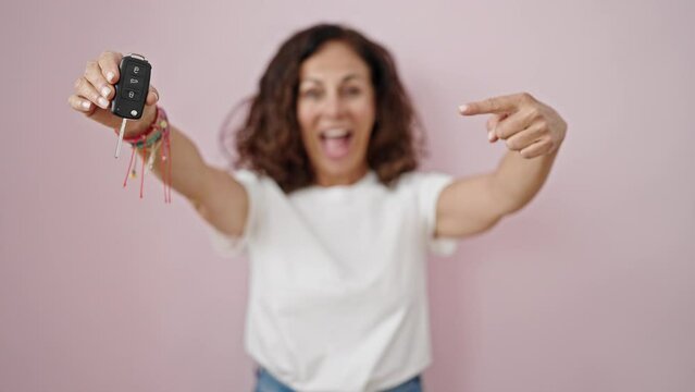 Middle age hispanic woman smiling confident pointing to key of new car over isolated pink background