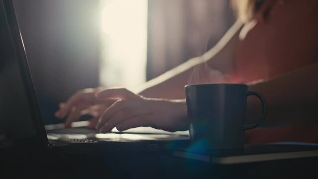 Close-up of a woman typing on a computer and then taking a cup of coffee. A business woman works at a laptop in the morning in her home office. High quality 4k footage