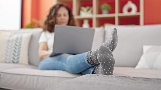 Middle age hispanic woman using laptop moving foot at clinic