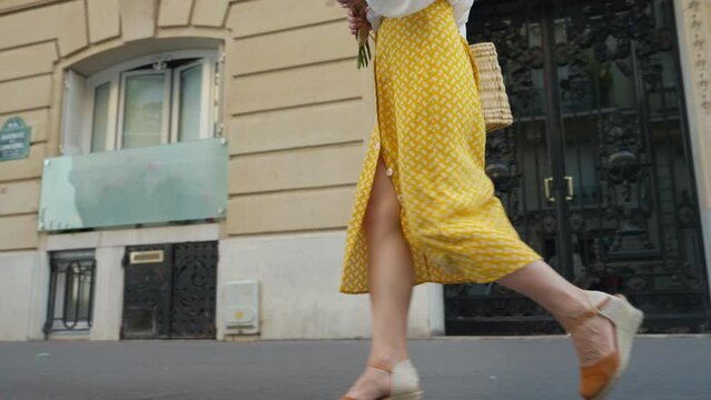 Young woman in a yellow skirt with a bouquet of flowers walking towards the Eiffel Tower on a spring day