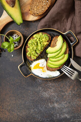 Healthy breakfast concept, sandwich with avocado and egg. Wholemeal bread toast sliced avocado and poached egg on a stone background. View from above. Copy space.