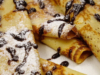 Freshly baked thin pancakes -crepes, folded in a triangle,  dressing in chocolate sauce and powdered sugar