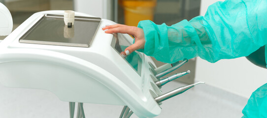 Female dentist hand is touching control screen of the patient chair in office.