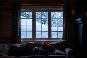 View through the window from cozy wooden cabin to snowy mountains during winter. Ski center...