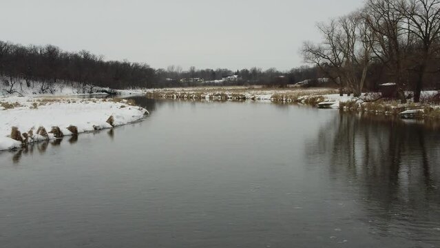Aerial shot follows a calm river flowing downstream in winter