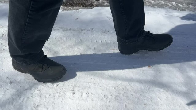 Low angle of man with black boots walking on a winter path