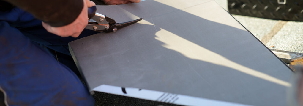 Banner mit Dach Bauklempner Handwerker bei der Arbeit auf dem Dach. Zink Bleche anzeichnen, zuschneiden und abkanten. Blechschere in der Hand des Facharbeiters.