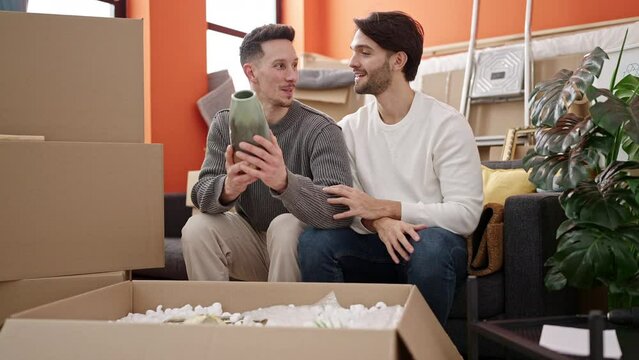 Two men couple unpacking cardboard box at new home