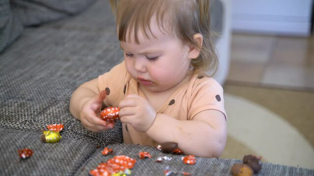 baby eats chocolate eggs. unwrapping candy. child eating candy